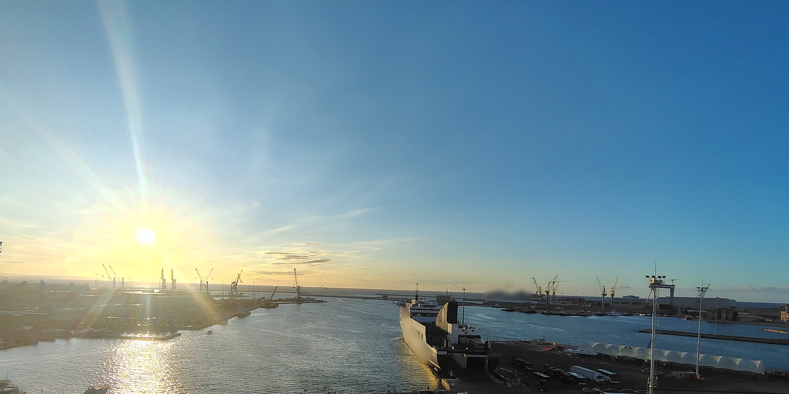 Ro-ro-alus laiturissa satamassa auringonnousun aikaan, taustalla nostureita